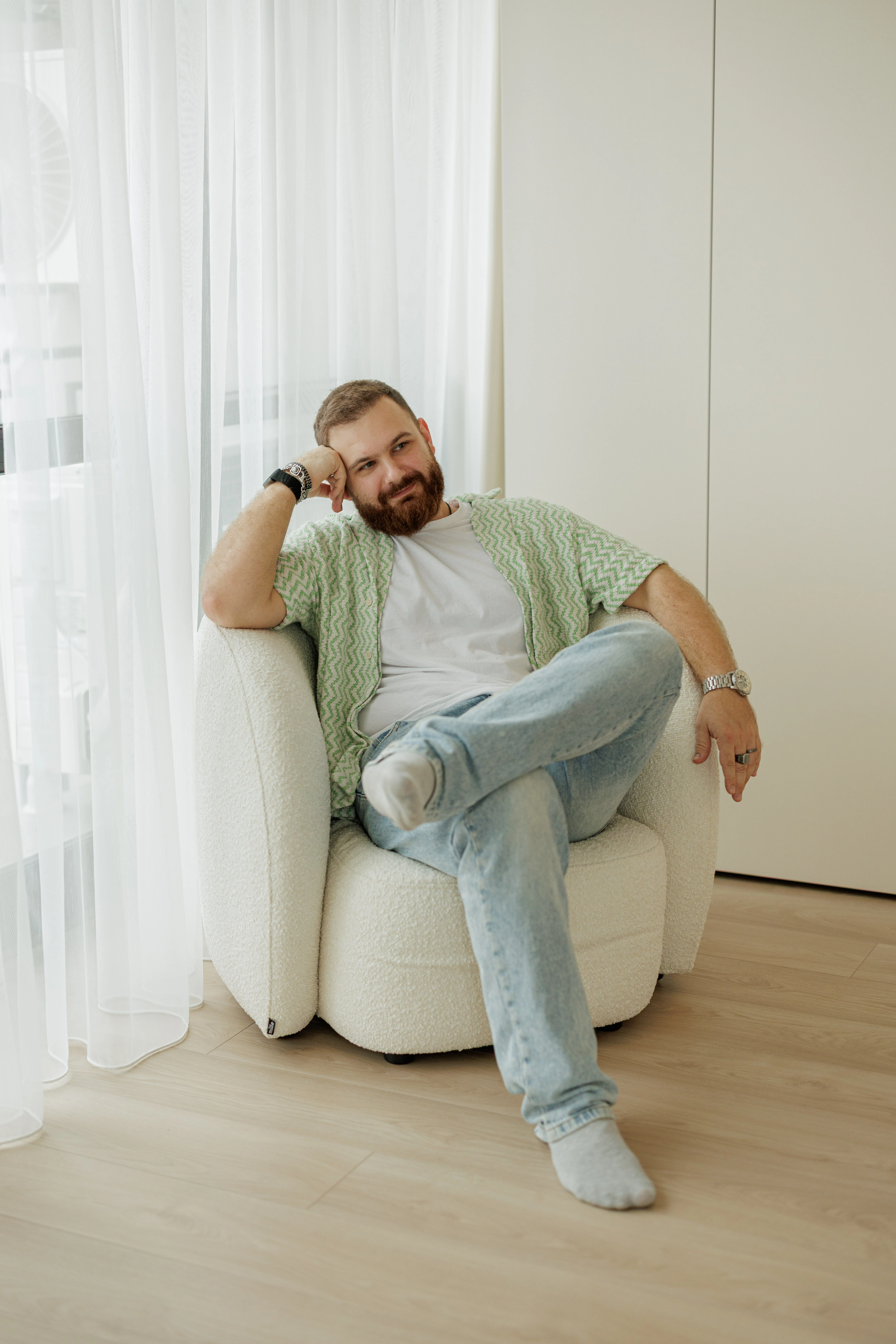 A man seated in a cream boucle Nuba armchair in an apartment, hand to his cheek