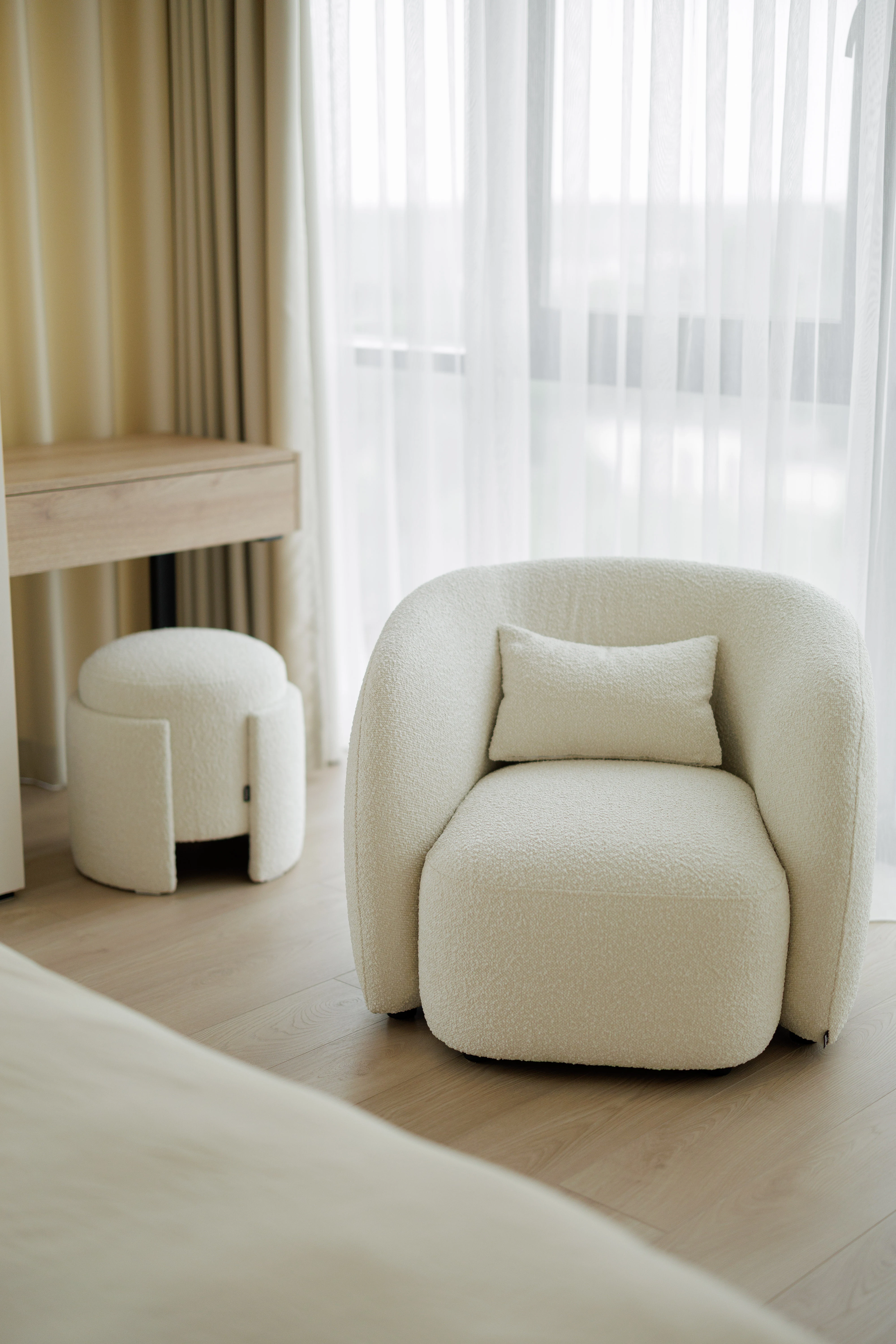 Cream bouclé Eden pouf beside a matching bouclé armchair by a bright window