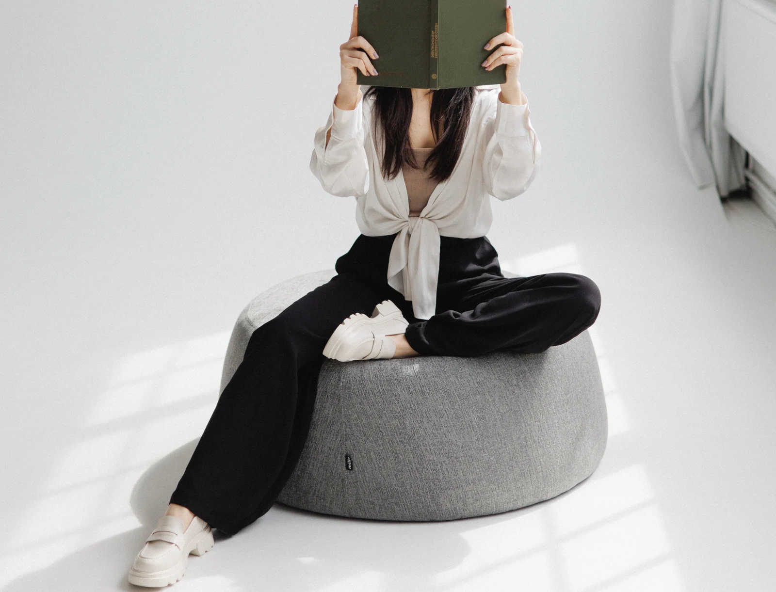 Woman seated on a grey linen Macarons pouf in a sunlit room
