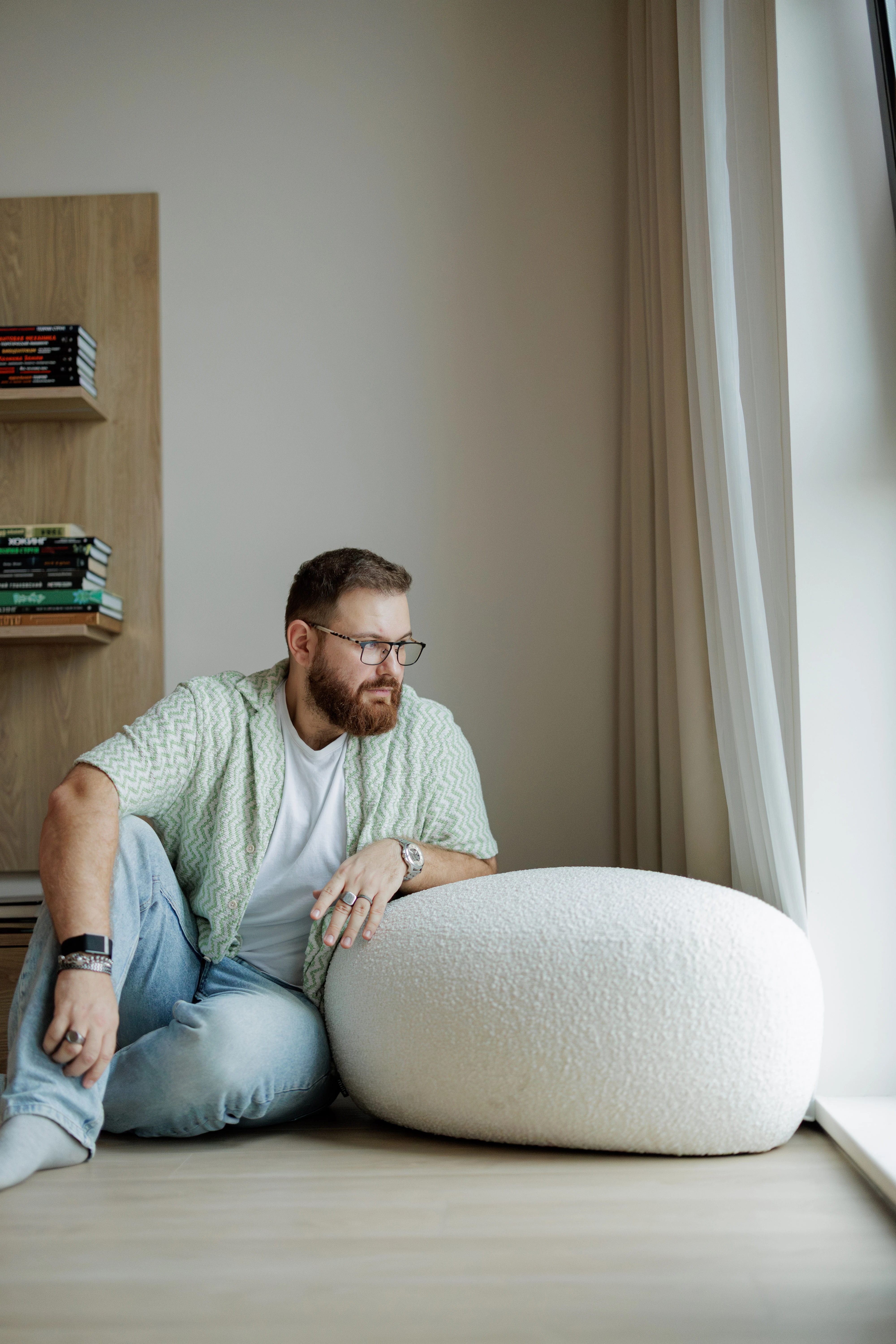 Cream bouclé Chios pouf in dramatic low light beside a curtained window