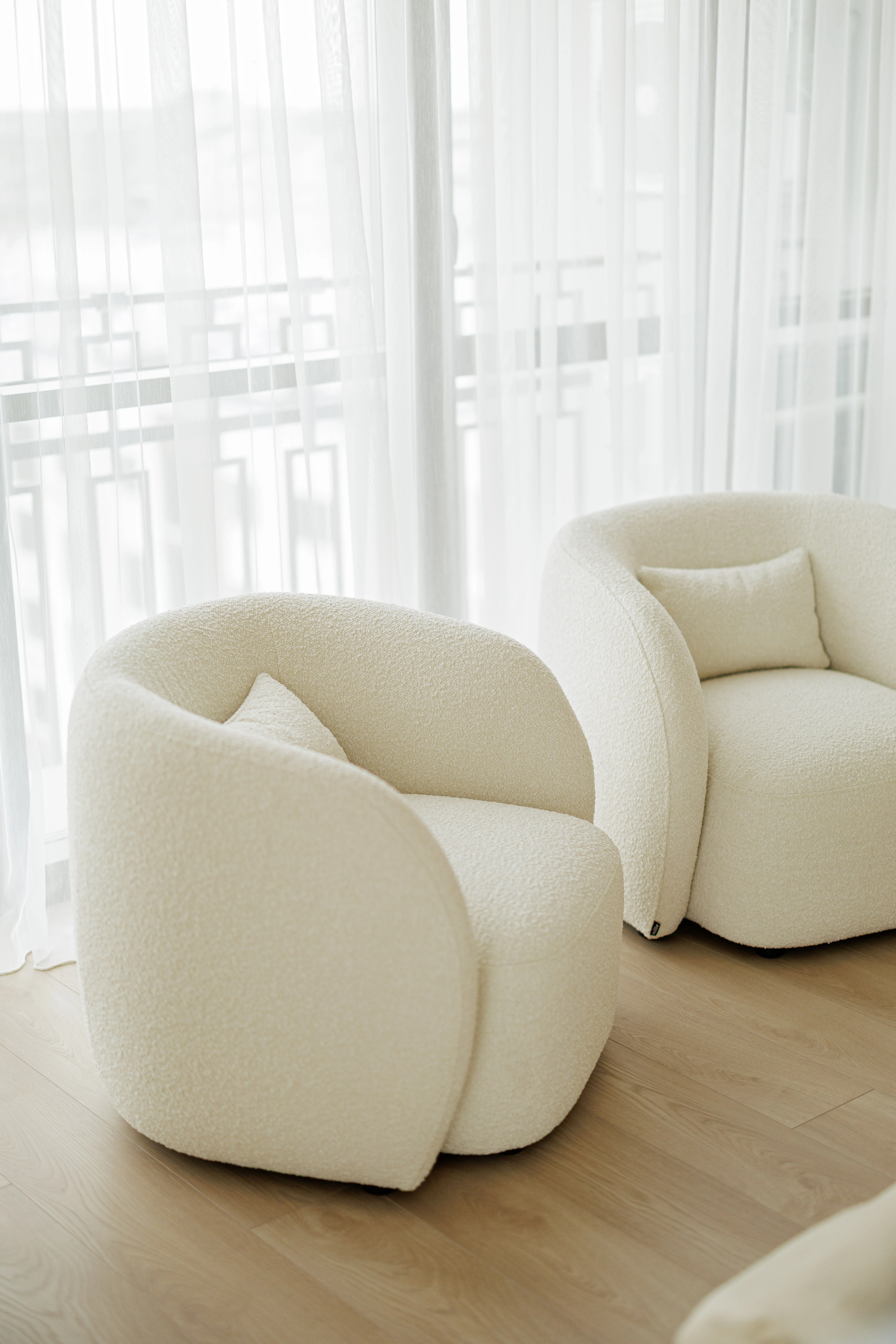 Two cream boucle Nuba armchairs together by a sheer-curtained window