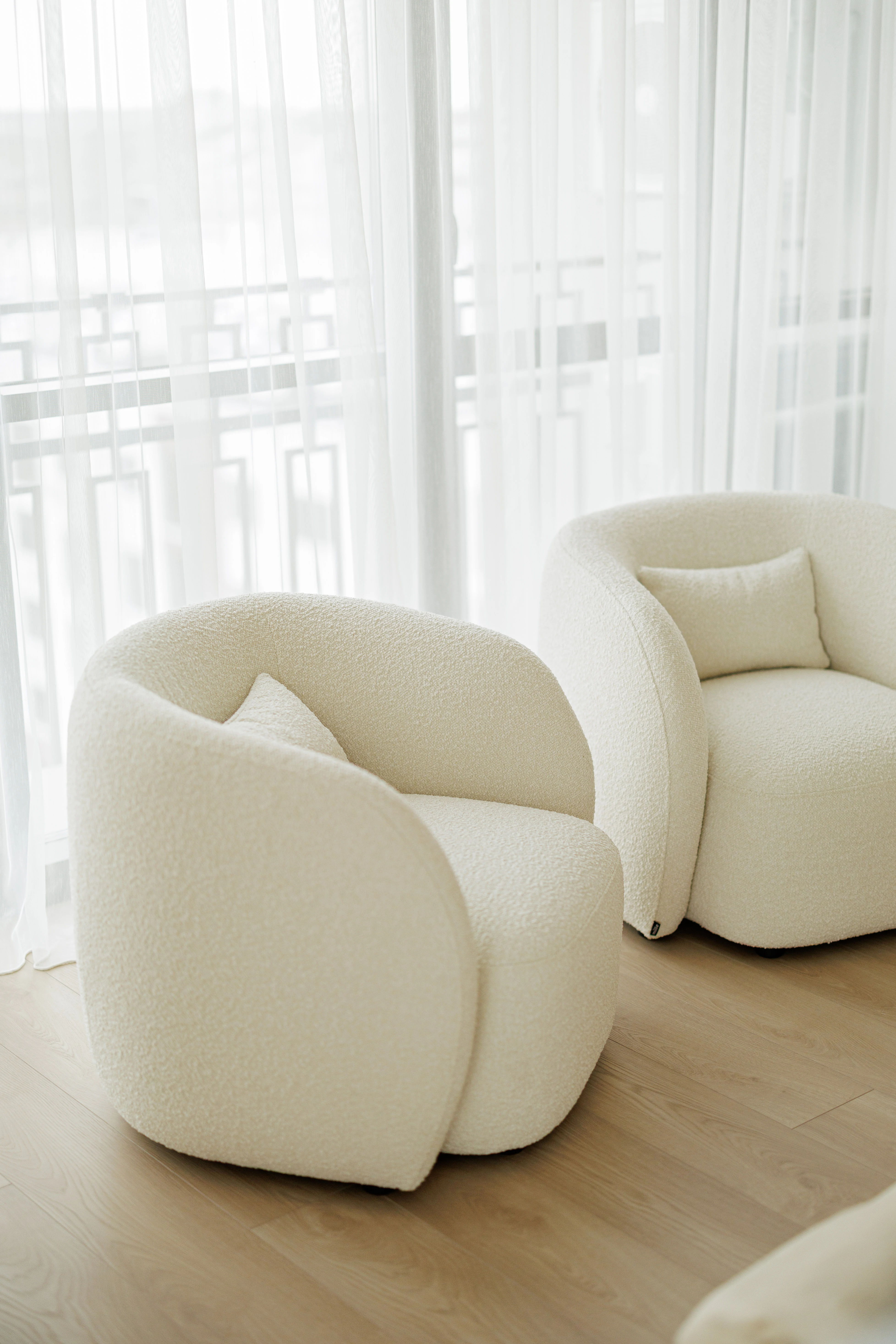 Two cream boucle Nuba armchairs side by side in front of a sheer-curtained apartment window