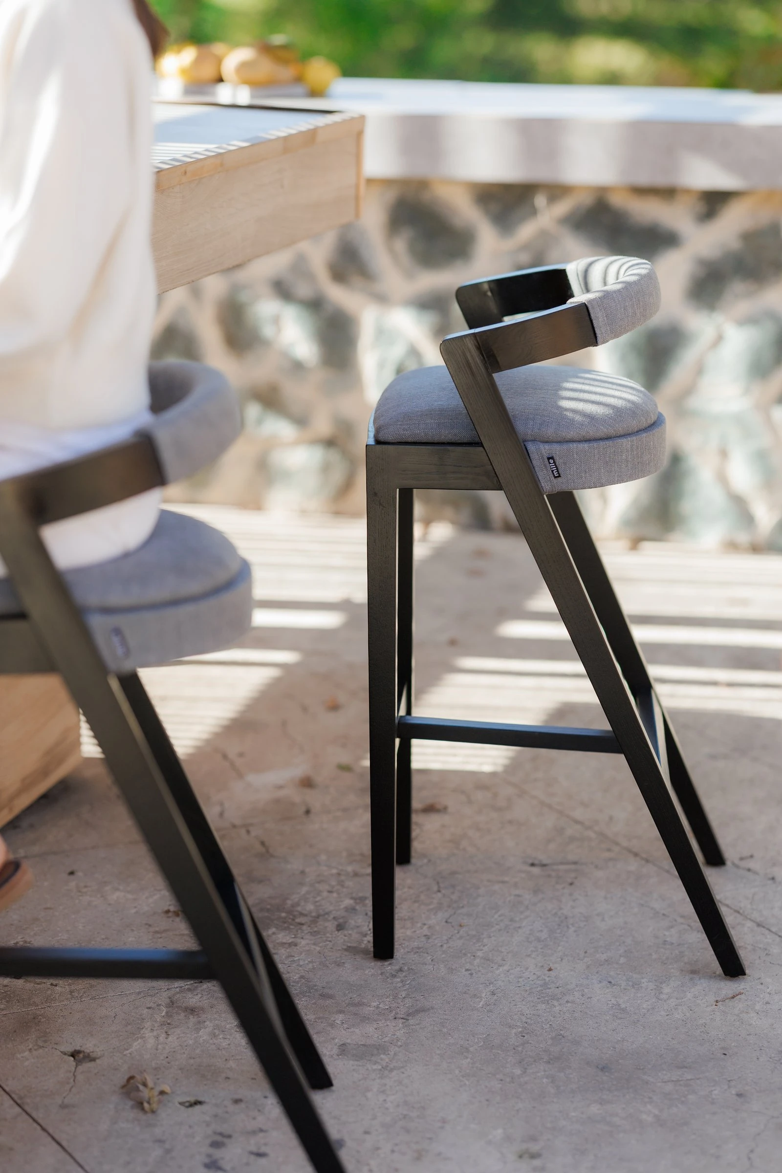Side angle of a Baffi bar stool at the villa counter showing the black-ash sawhorse frame