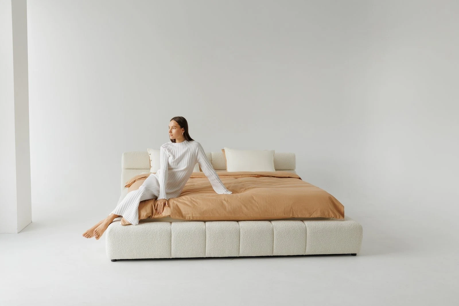 Cream boucle Nao with a model seated at the foot of the bed, white striped robe