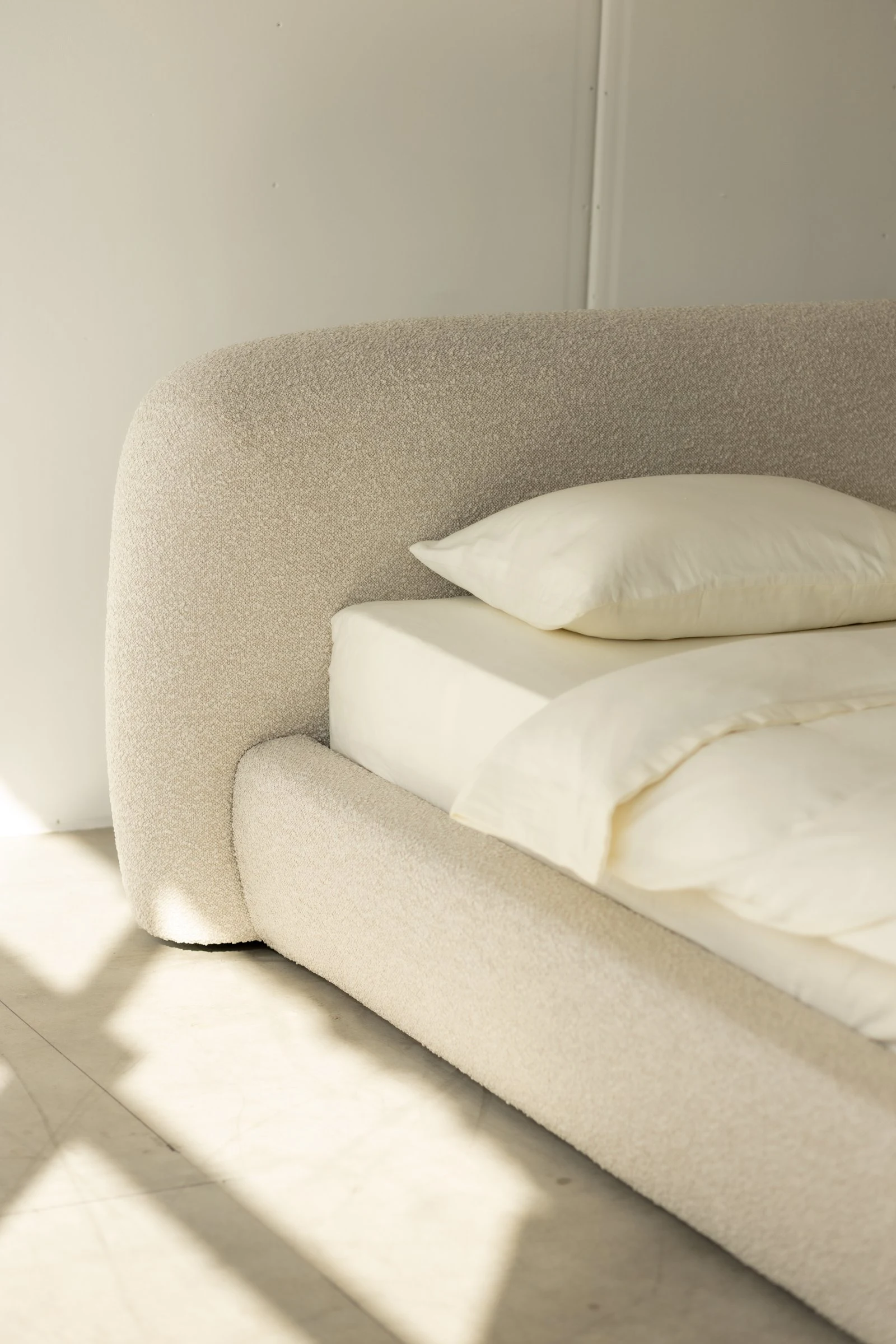 Detail of the Belagio headboard corner curving down toward the bed frame in cream boucle