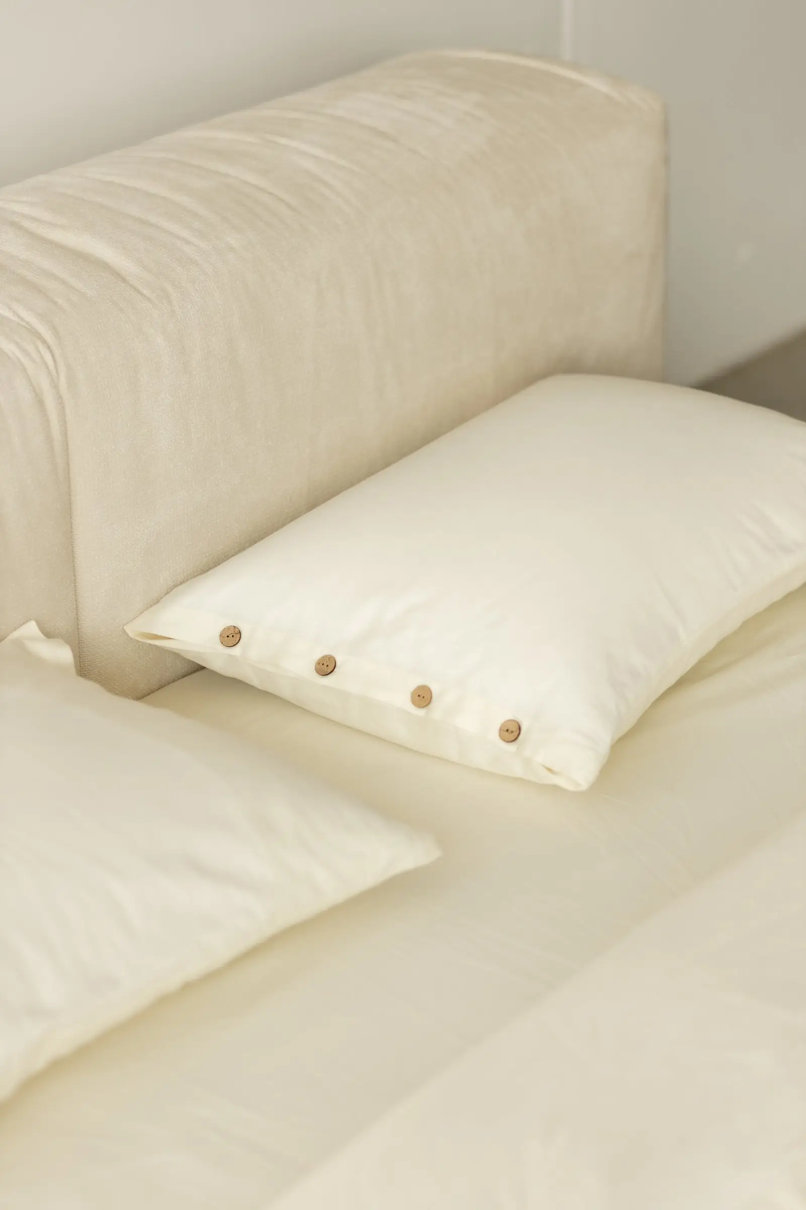 Two white pillows with a coconut-button row in front of the cream Marmaris slouchy headboard