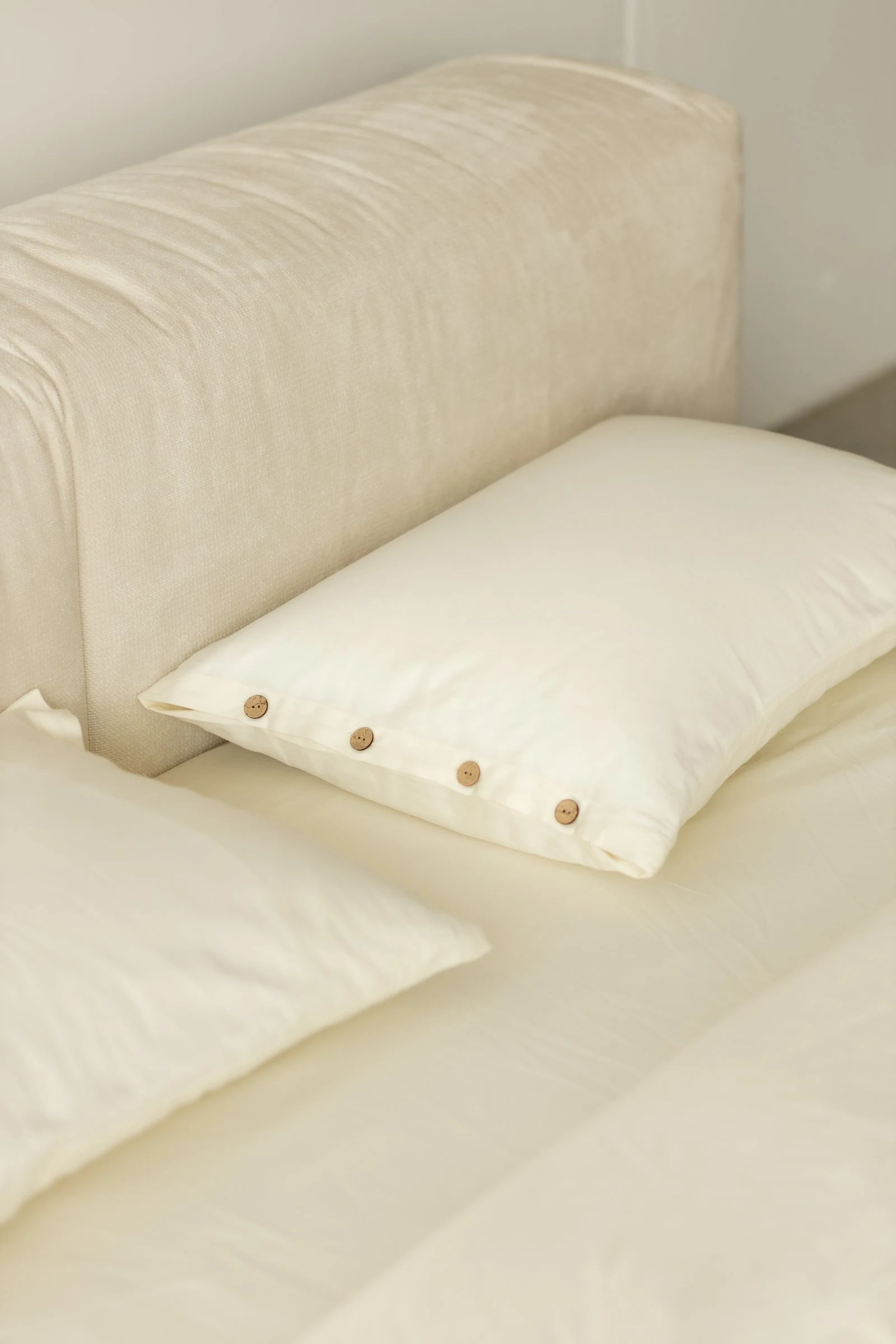 Two white pillows with a coconut-button row in front of the cream Marmaris slouchy headboard