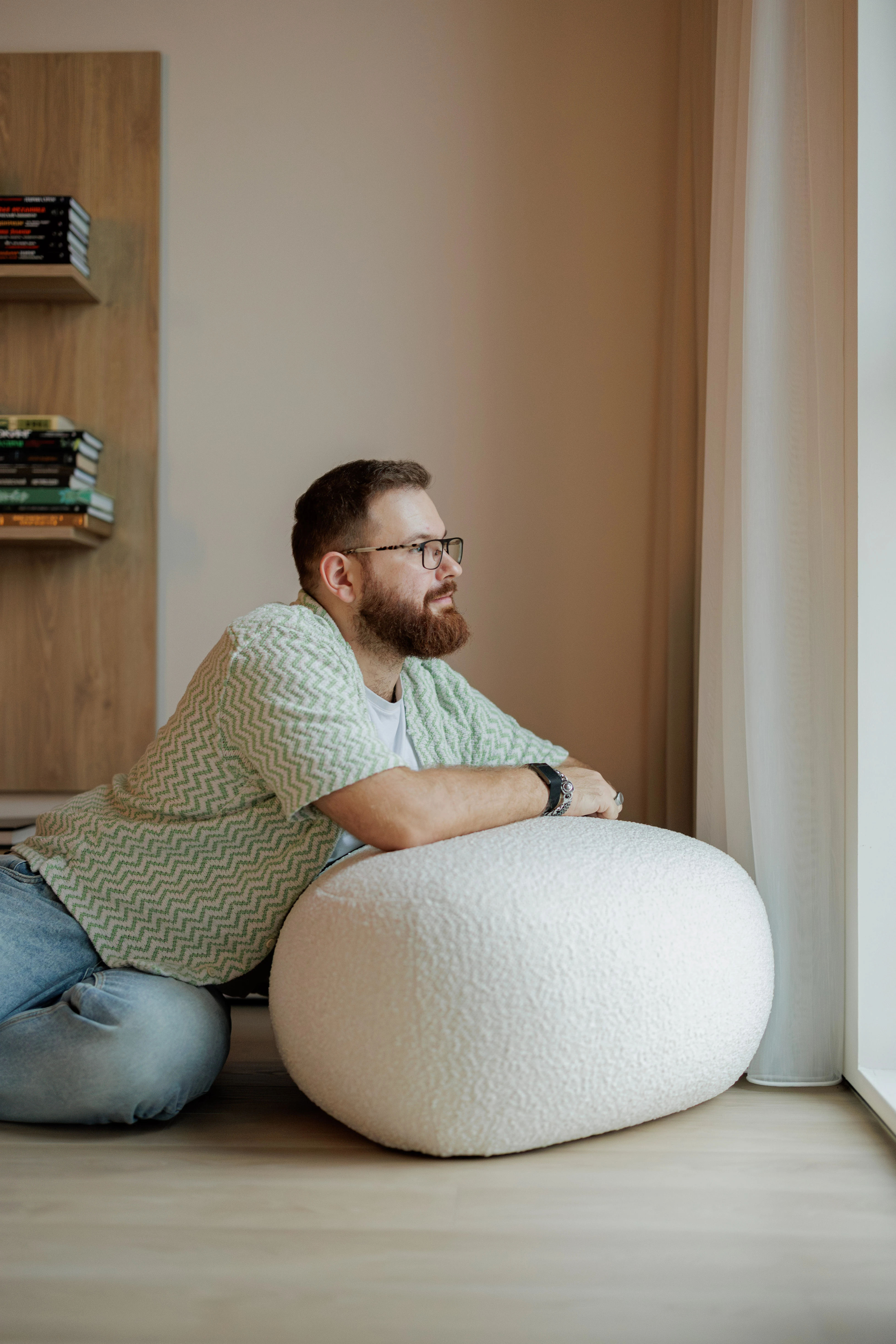 A man leaning on a cream bouclé Chios pouf by a window