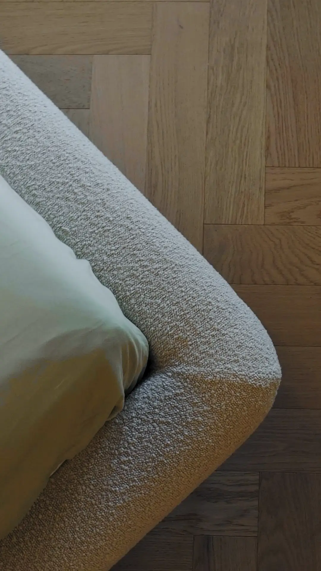 Macro of the cream boucle Fresco bed foot corner resting on herringbone parquet wood floor