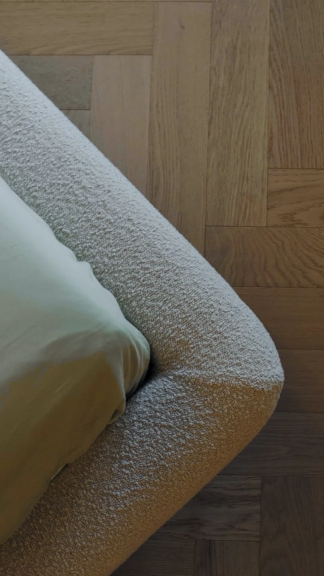 Macro of the cream boucle Fresco bed foot corner resting on herringbone parquet wood floor
