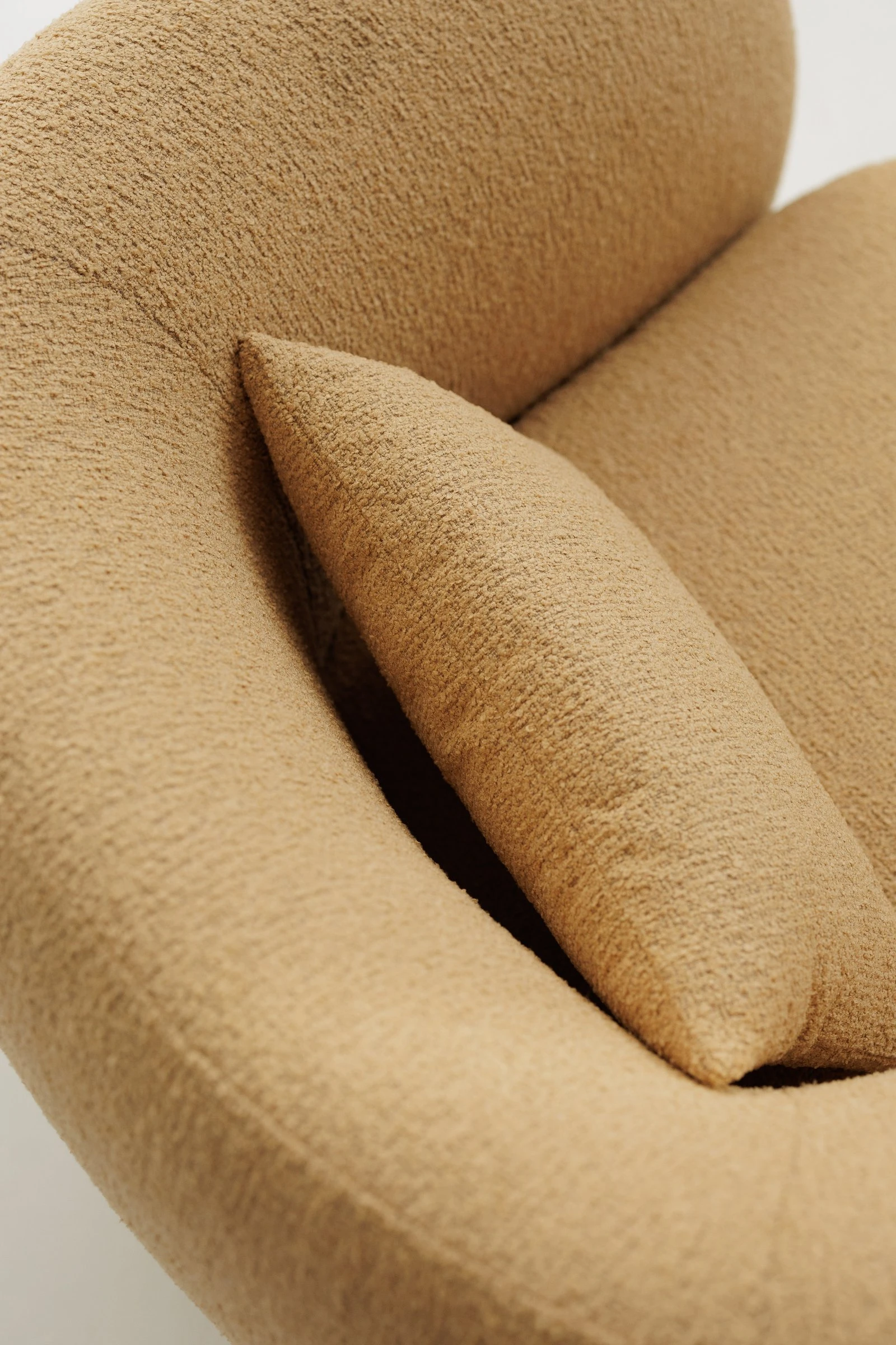 Three-quarter view of the mustard boucle Nuba armchair showing the wraparound back