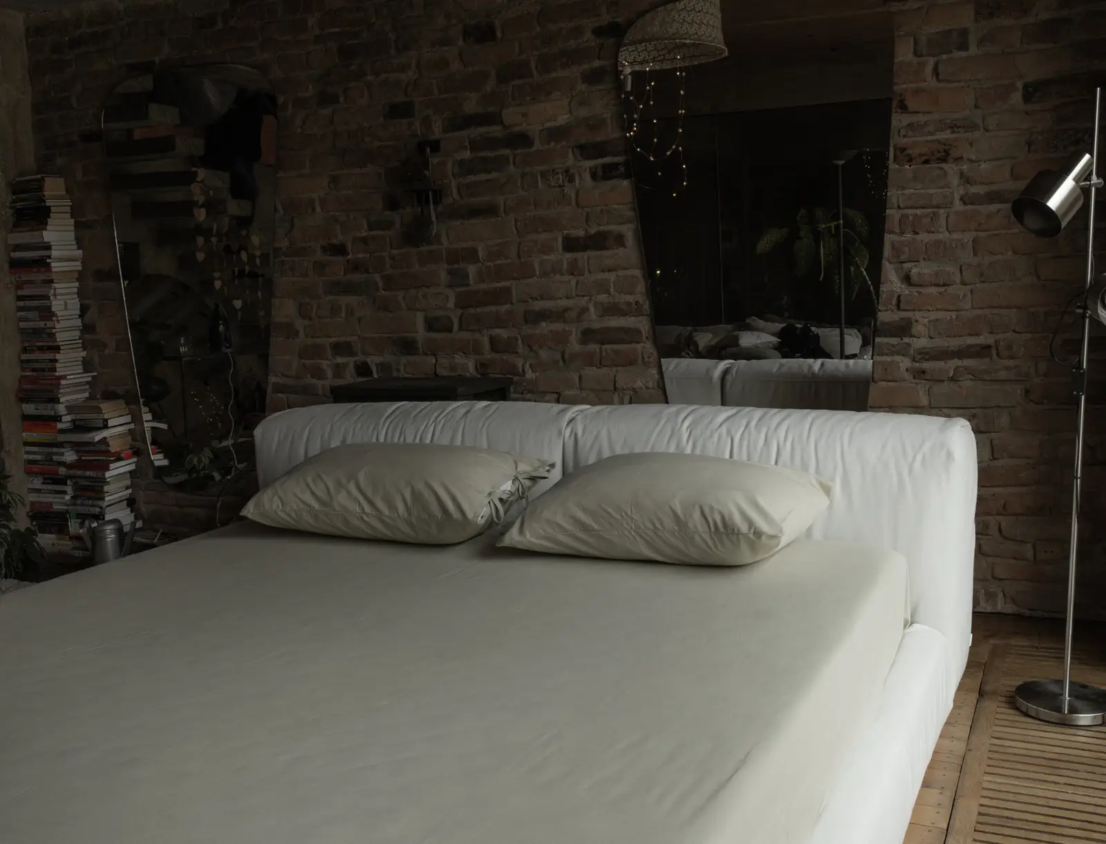 Side view of the Marmaris in a rustic brick loft with a tall mirror leaning behind the bed and a stack of books