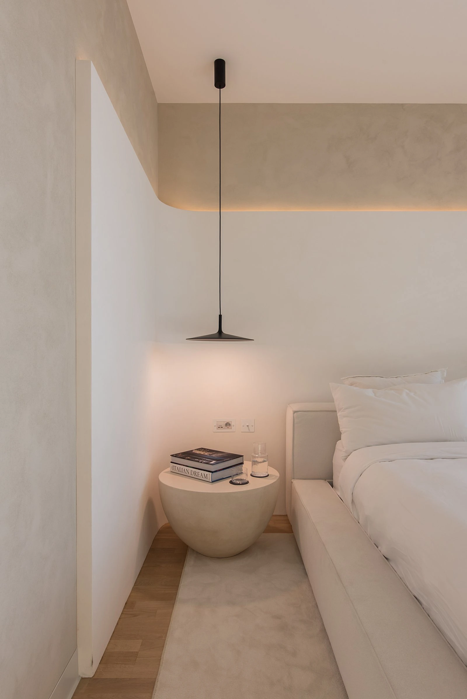 Pebble-shaped concrete side table beside the cream Palermo with an open book and a glass of water on top