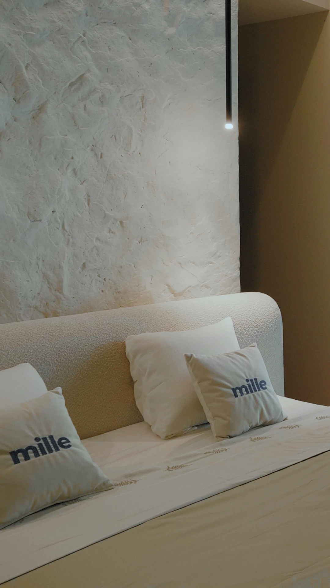 Vertical detail of the cream Fresco arched headboard against a textured plaster wall with Mille pillows in front