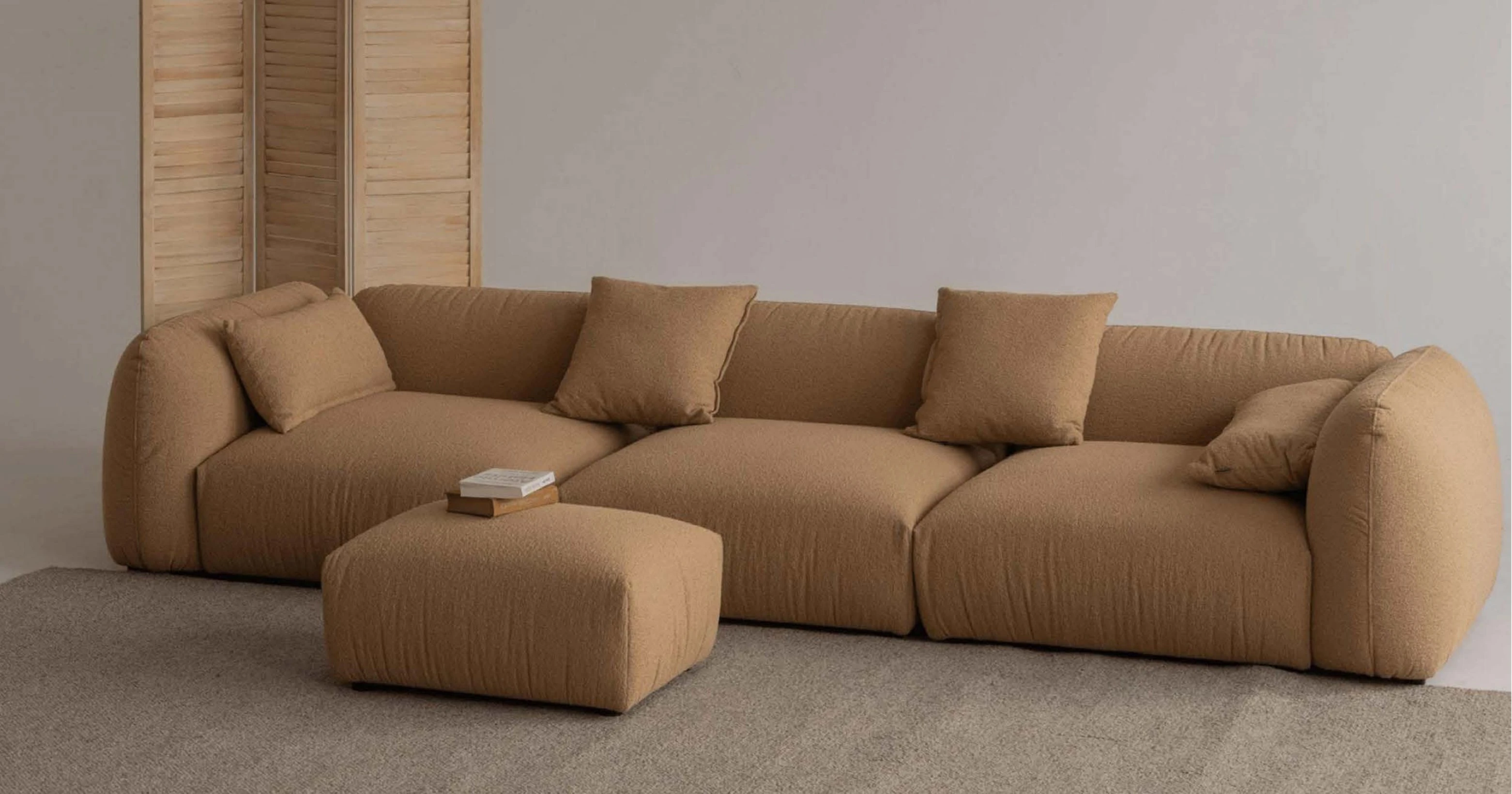 A camel boucle Tesa sectional with rolled arms and a matching ottoman on a wool rug.