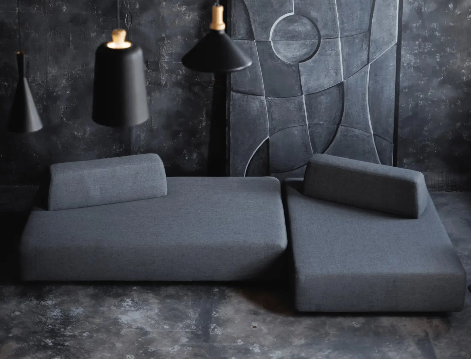Charcoal Deseda against a textured concrete wall with pendant lamps and a sculptural art panel