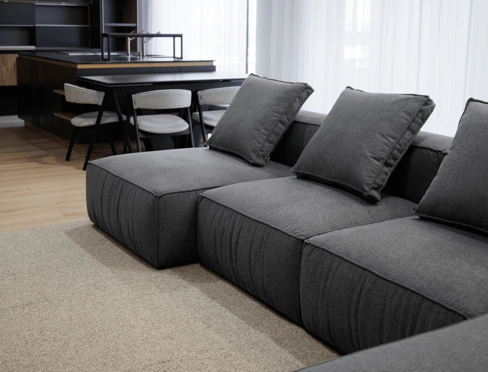 Charcoal Milano sectional next to a dining setting with sheer curtains and a houseplant