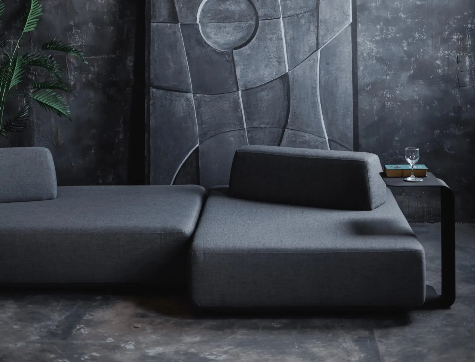 Charcoal Deseda in a dark concrete room with a tall industrial window and a leaning art panel