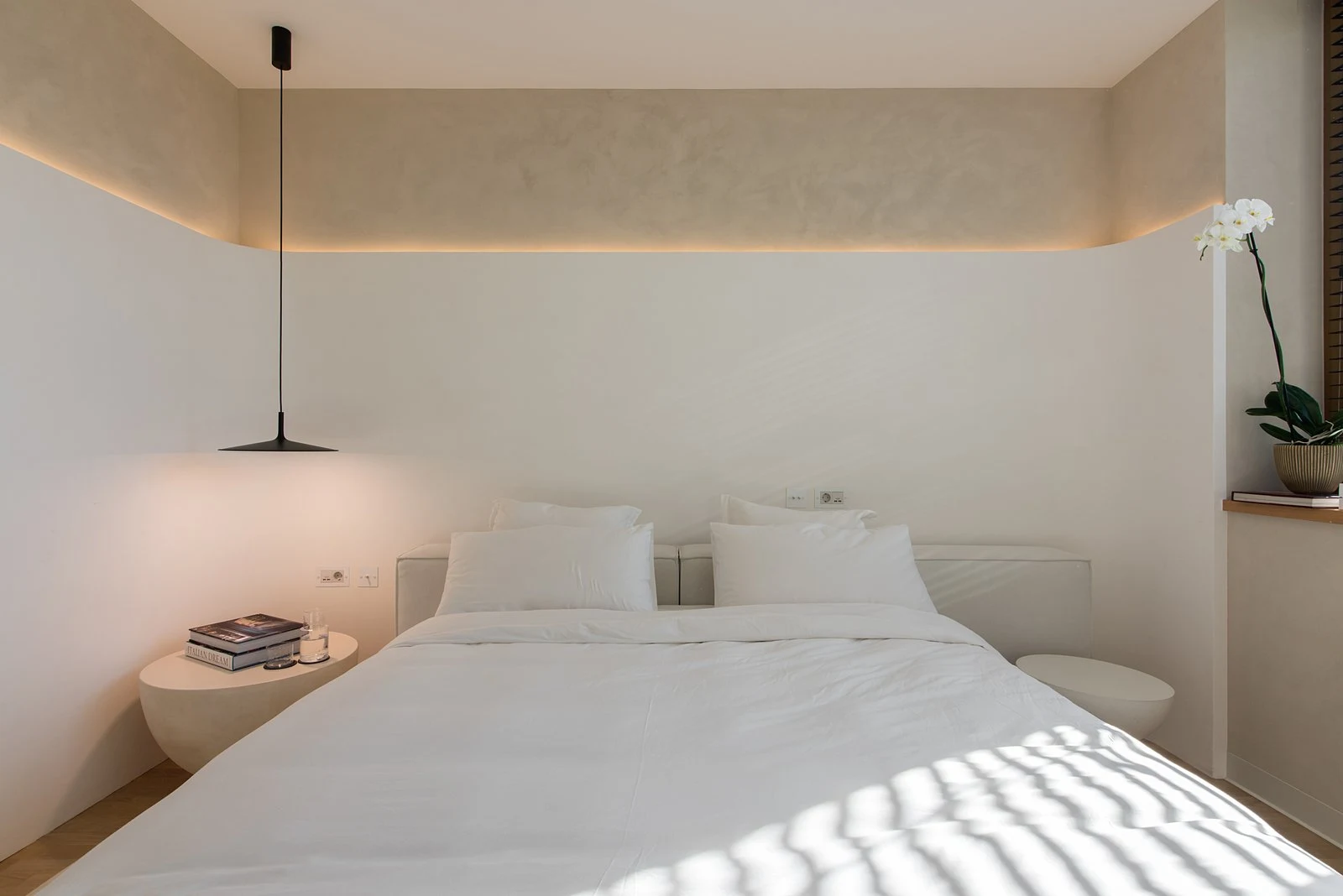 Cream Soho 800 Palermo bed in a light bedroom with twin pebble side tables, a single black pendant lamp and an orchid