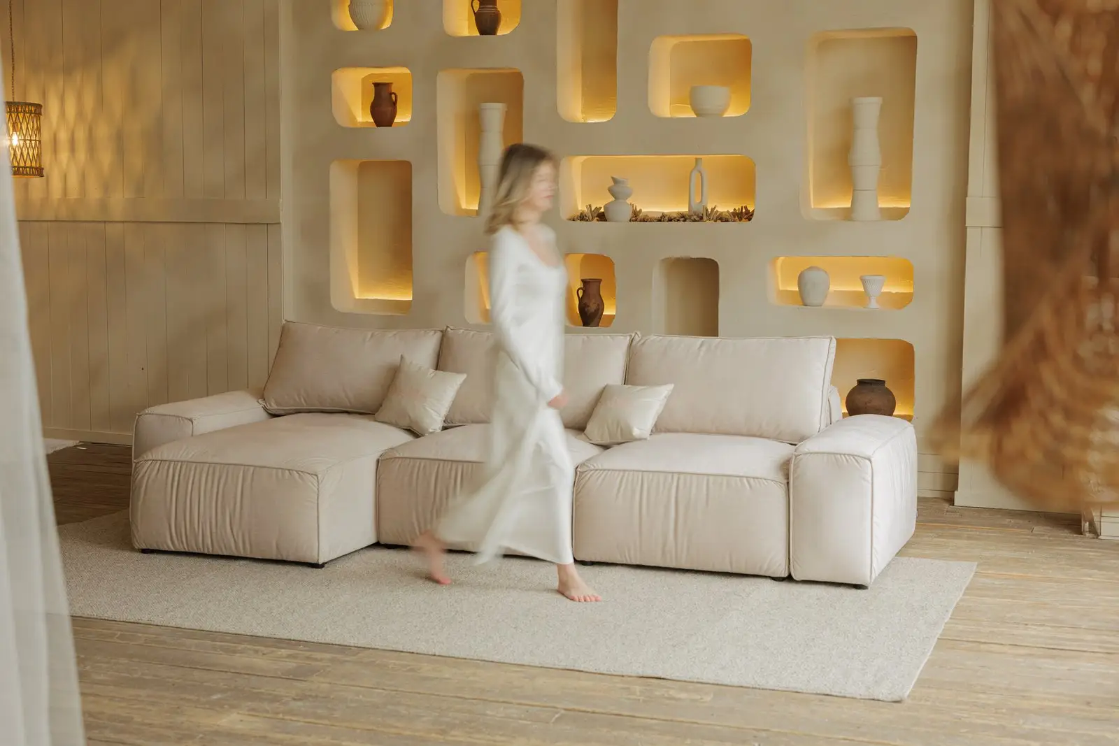 Cream Milano with a woman walking past in a long white dress, a wall of lit niches behind