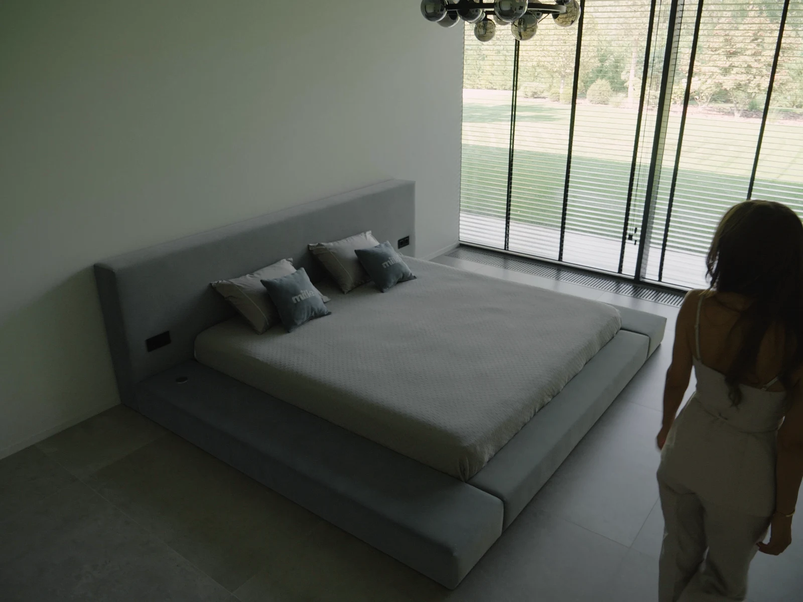 A grey velvet slim-configuration Connect bed in a minimalist concrete-floor bedroom with floor-to-ceiling windows opening onto a garden