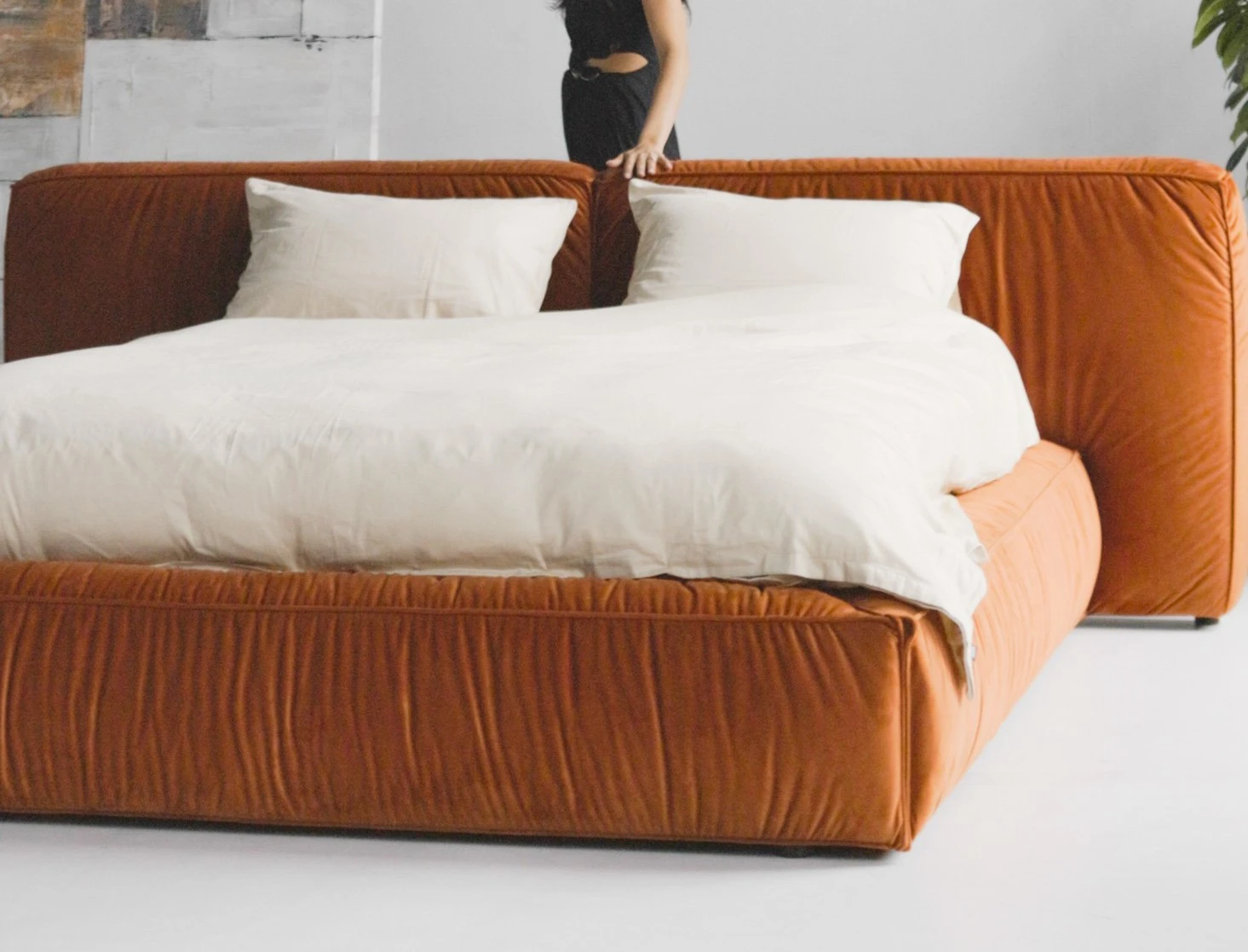 Burnt-orange velvet Palermo in a high-ceilinged loft with industrial windows, model in a black dress seated on the bed