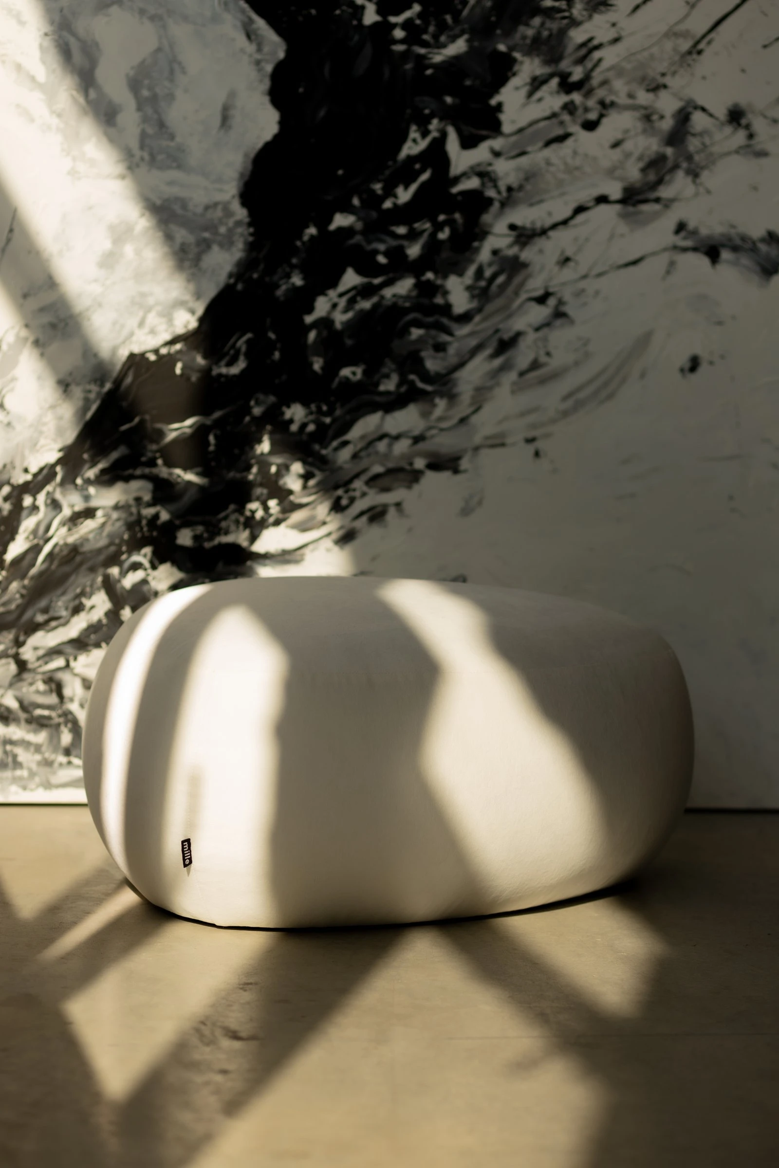 Cream velvet Chios pouf against a marble wall with dramatic linear shadows
