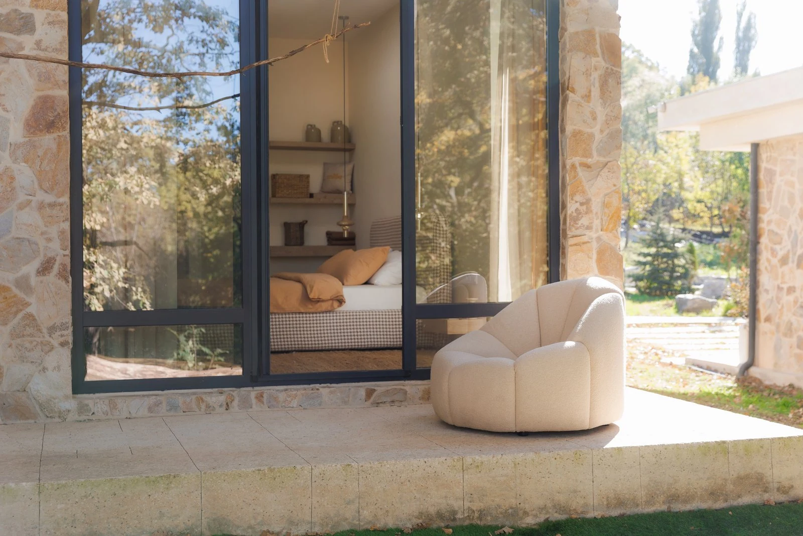 Cream Flora chair on a stone-walled villa patio with golden autumn trees and a bedroom visible through the glass behind
