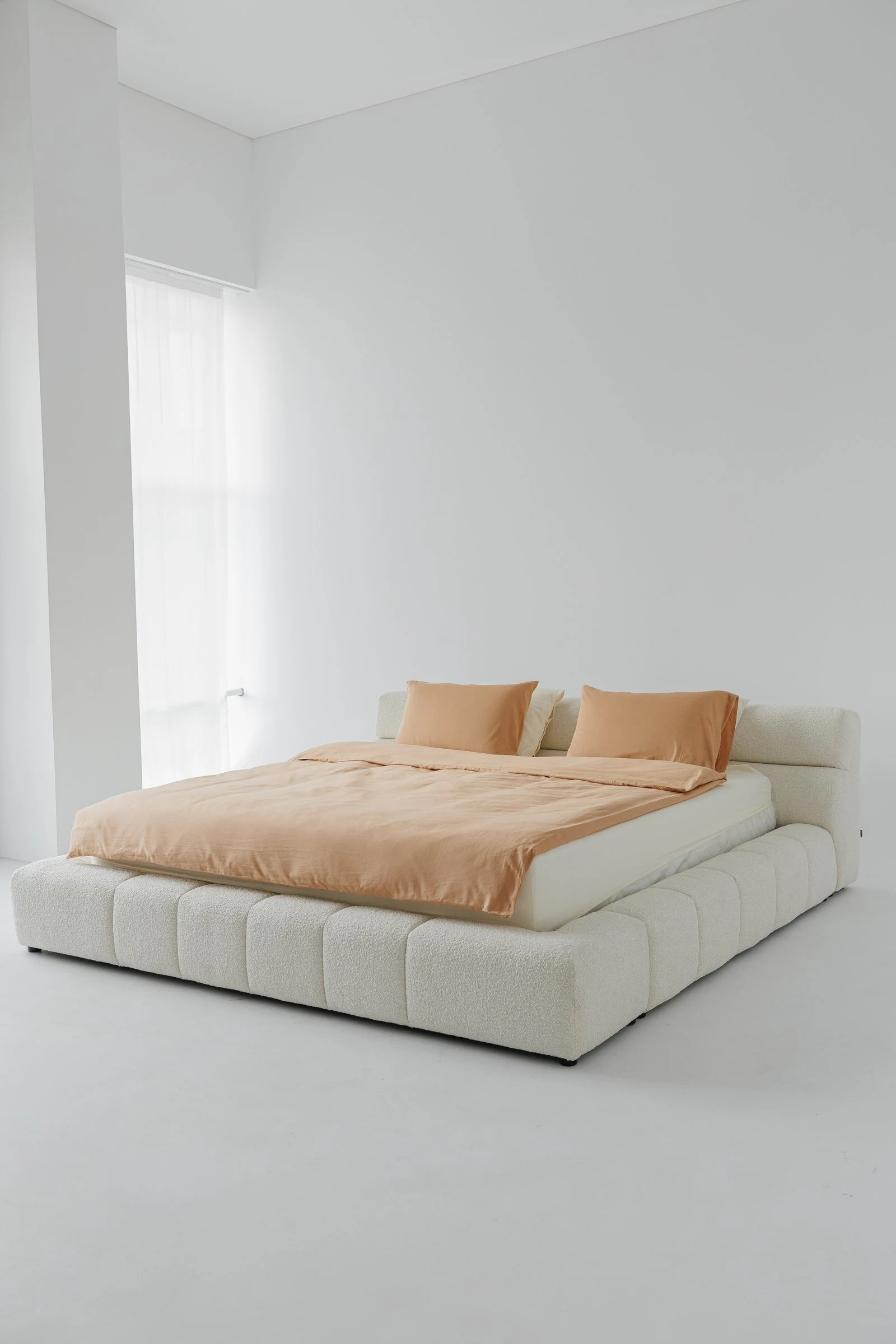 Cream boucle Nao bed in a bright minimal white room with peach bedding