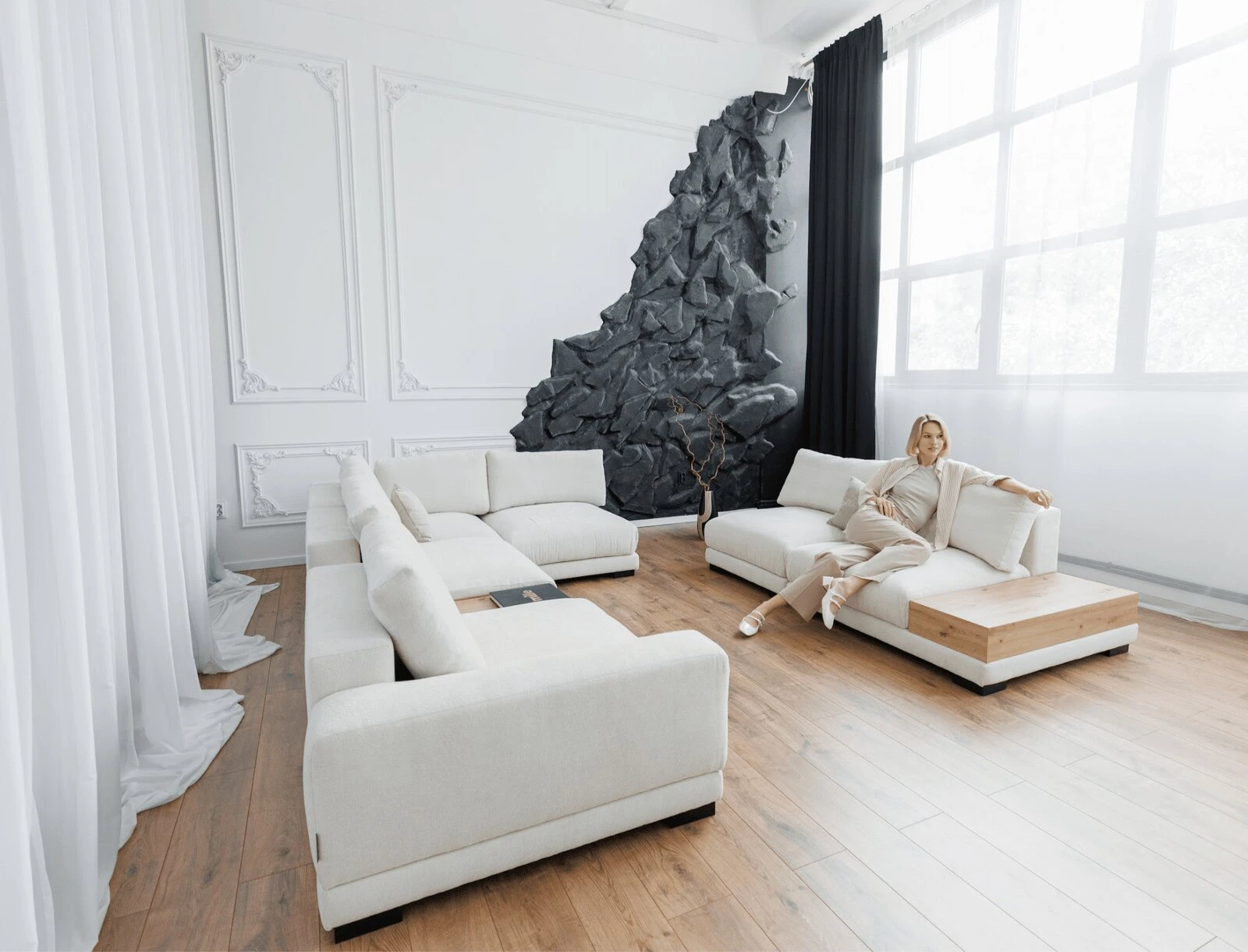 Two cream Palermos in a room with a stone-art feature wall, with a woman lounging on the second sofa
