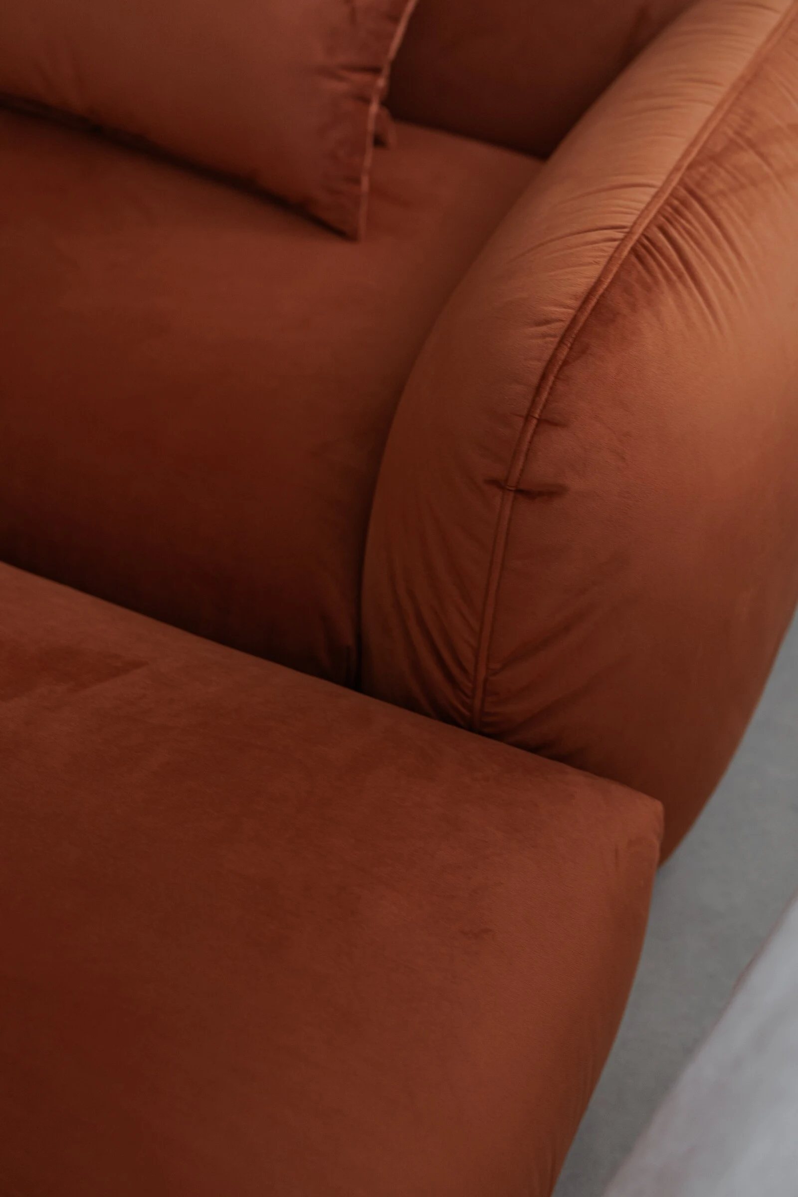 Macro detail of the rust velvet Tesa armrest and cushion with light raking across the pile