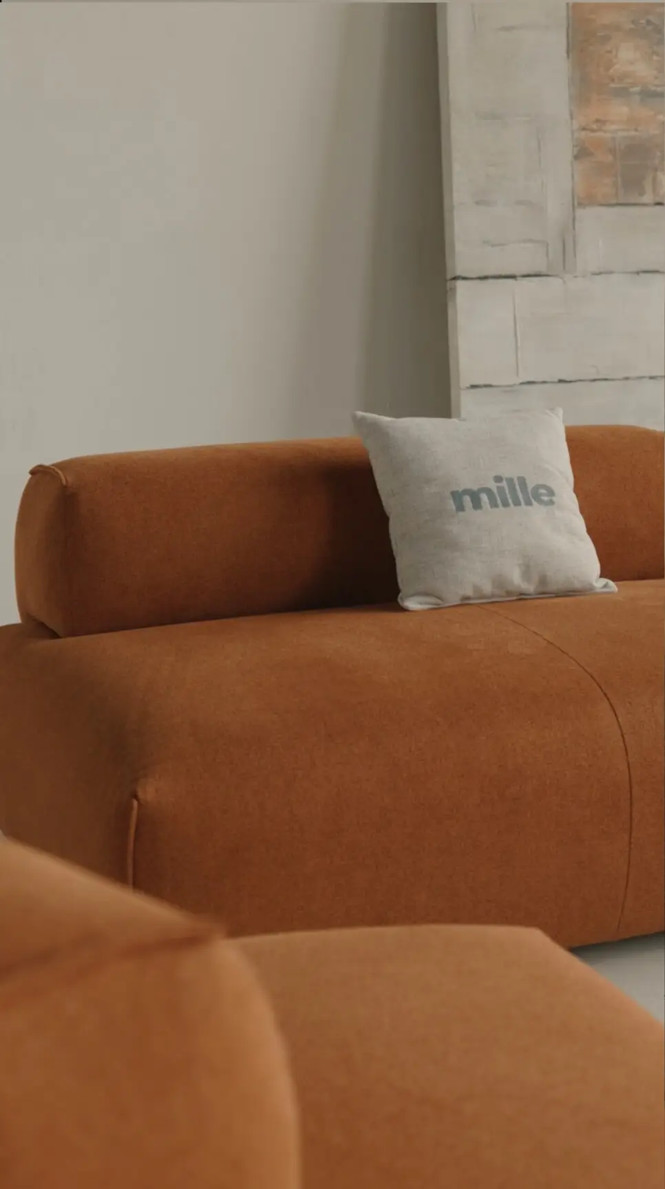 Close detail of the rust Nissa with a Mille pillow against an abstract art panel