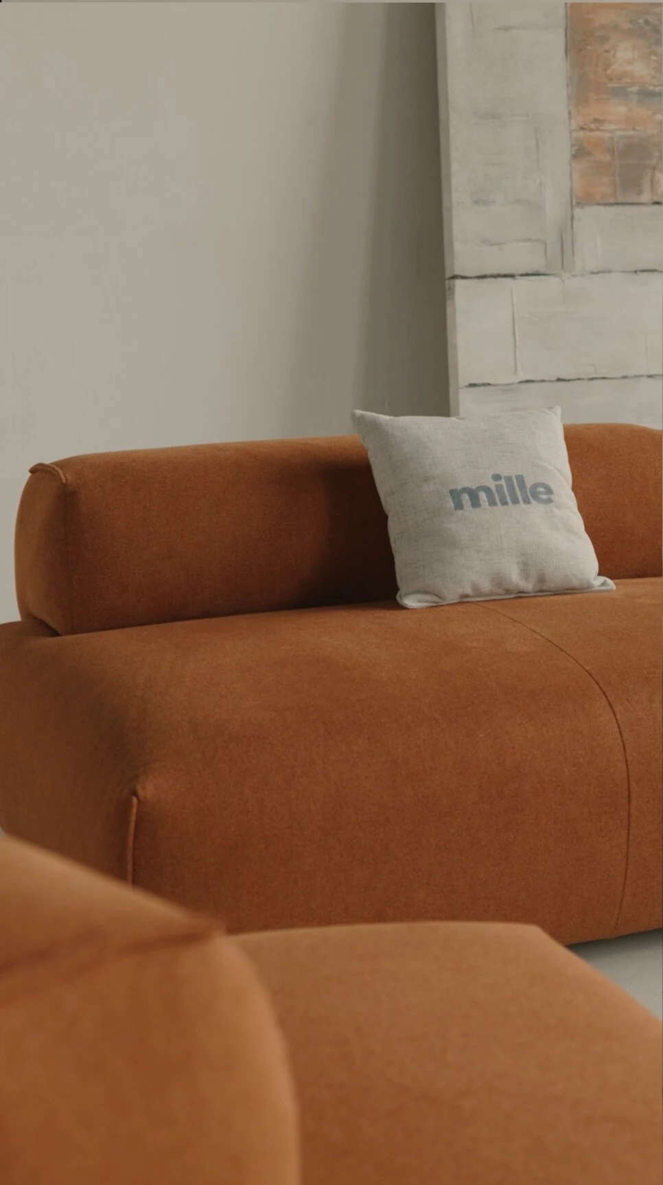 Close detail of the rust Nissa with a Mille pillow against an abstract art panel