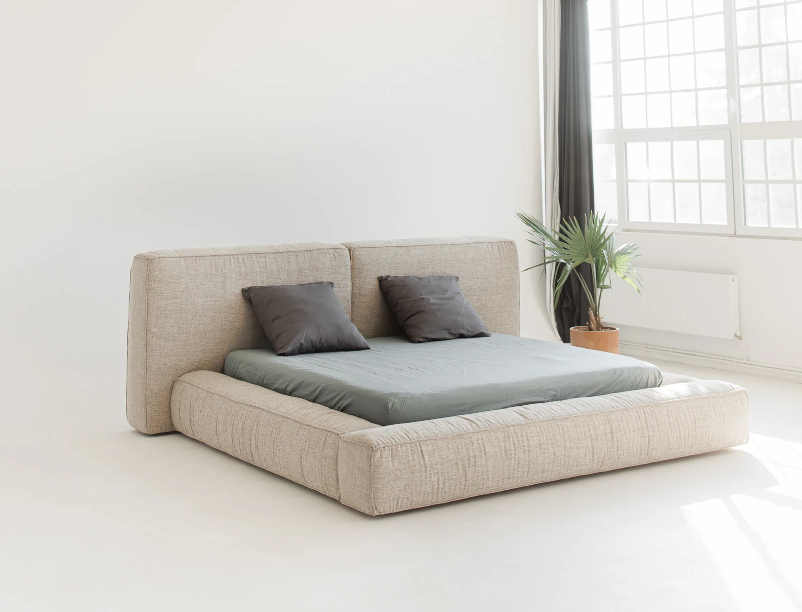 Sand linen-look Palermo bed in a bright minimal studio with a plant by the window and two grey pillows on the bed