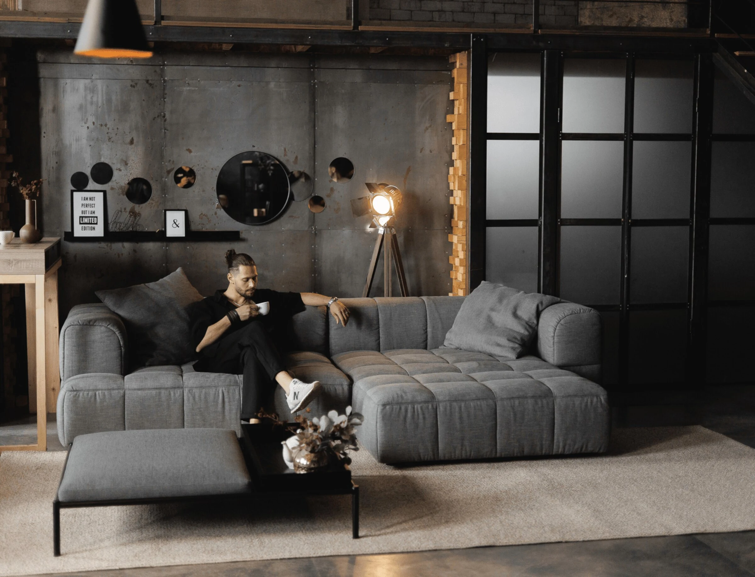 Charcoal grey Soft modular in an industrial loft, a man drinking coffee, Edison-lamp lighting and concrete walls