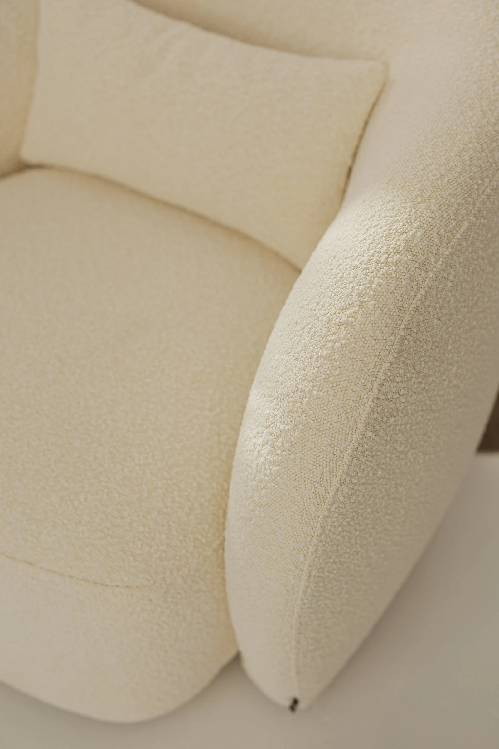 Three-quarter view of the white boucle Nuba armchair showing the wraparound back curving from one side to the other in a single continuous form